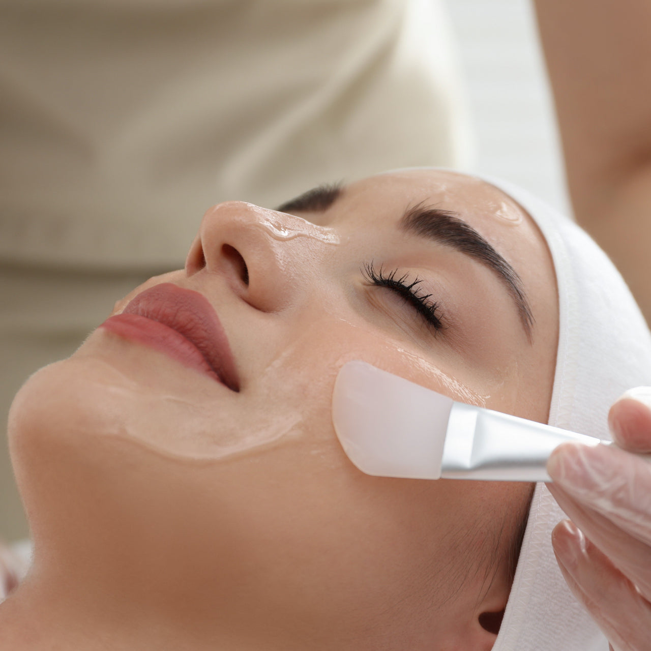 Person receiving a facial treatment with a brush applying cream to their face.